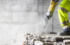 A construction worker strikes concrete with a hammer, demonstrating manual labor on a construction site.
