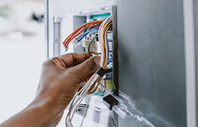 A hand connecting colored wires to a control panel inside an appliance.