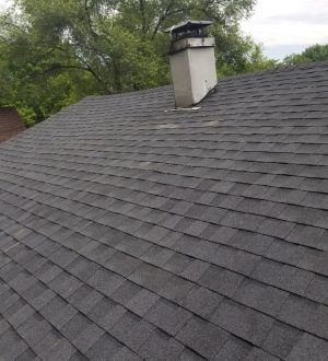 A house roof featuring a prominent chimney against a clear sky.