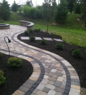 A stone walkway bordered by lush landscaping and trees, creating a serene outdoor pathway.