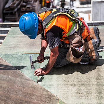 A man wearing a hard hat and safety vest works on a construction site, using tools and overseeing building progress.