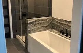 Modern bathroom featuring a sleek bathtub with a marble surround, a glass shower enclosure, and stylish black fixtures.