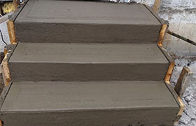 Freshly poured concrete steps, three levels high, with wooden forms outlining the edges, ready for curing.